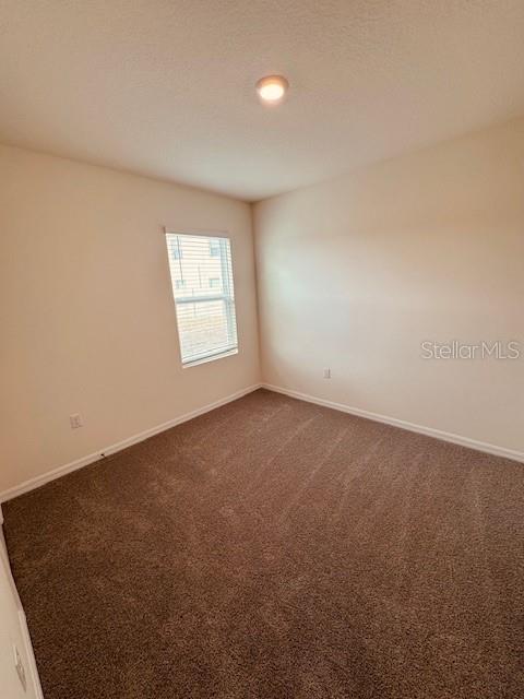 unfurnished room featuring dark carpet and baseboards