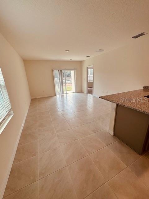 unfurnished room with visible vents, a textured ceiling, baseboards, and light tile patterned floors