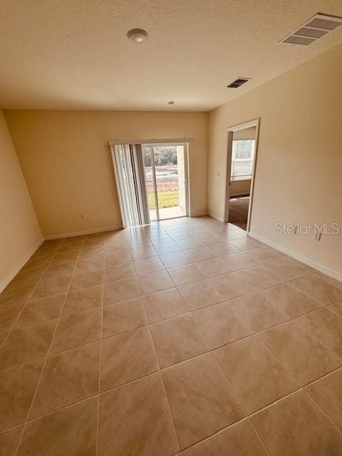 empty room with light tile patterned floors, baseboards, visible vents, and a textured ceiling