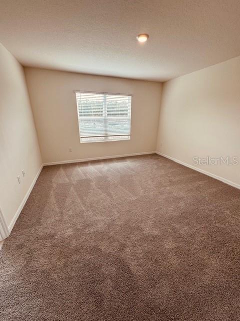 carpeted spare room featuring a textured ceiling and baseboards