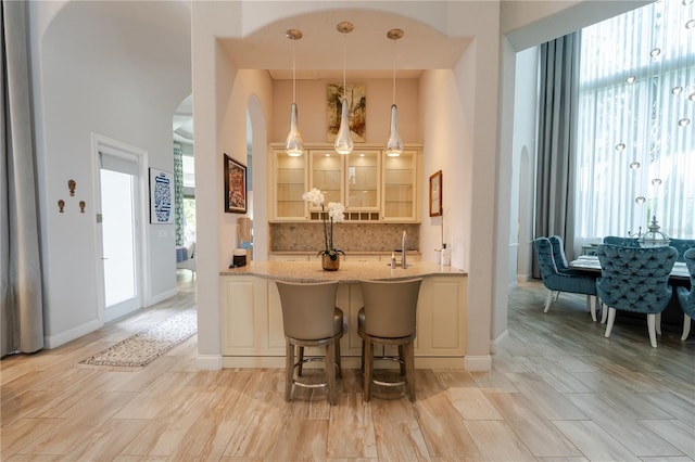 bar featuring light stone countertops, sink, hanging light fixtures, light hardwood / wood-style floors, and decorative backsplash