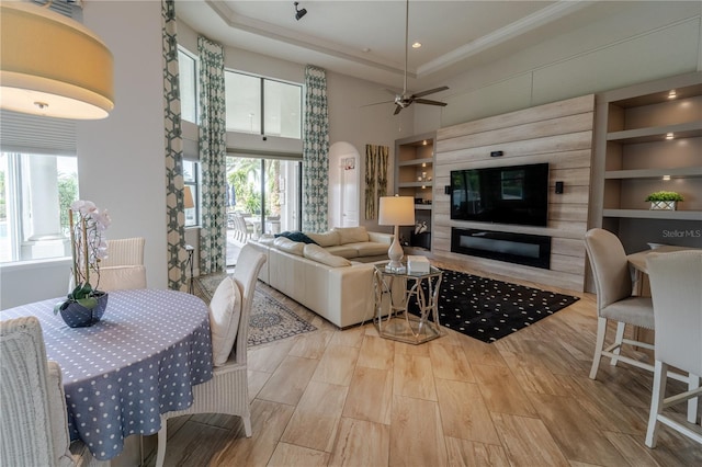 living room featuring a tray ceiling, ceiling fan, built in features, and light wood-type flooring