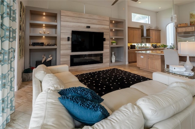 living room featuring built in shelves, a towering ceiling, light tile patterned floors, and ceiling fan