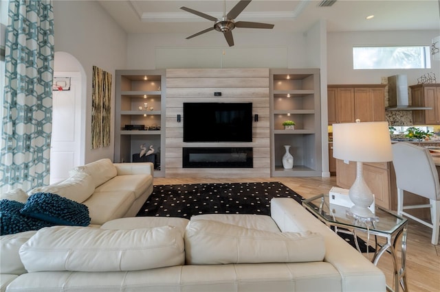 living room with a towering ceiling, ornamental molding, ceiling fan, built in features, and light hardwood / wood-style floors