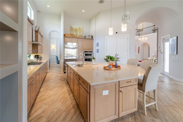 kitchen with a kitchen island with sink, a high ceiling, hanging light fixtures, sink, and a chandelier