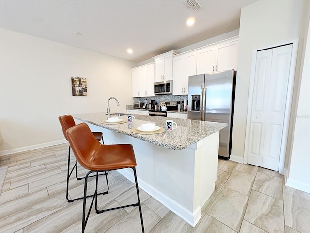 kitchen with a center island with sink, white cabinets, light stone countertops, appliances with stainless steel finishes, and a kitchen bar