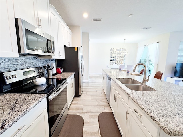 kitchen with white cabinetry, sink, stainless steel appliances, decorative light fixtures, and a kitchen island with sink