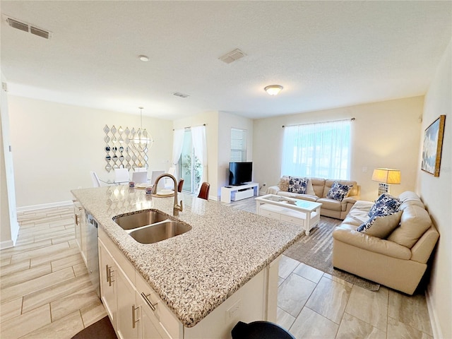 kitchen with light stone counters, sink, white cabinets, hanging light fixtures, and an island with sink