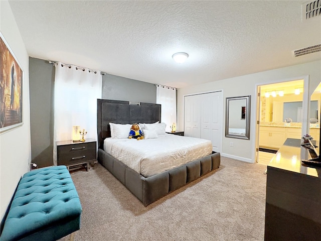 bedroom with ensuite bathroom, a textured ceiling, light carpet, and a closet