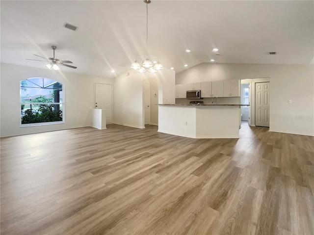 kitchen featuring lofted ceiling, white cabinets, kitchen peninsula, hanging light fixtures, and light hardwood / wood-style flooring