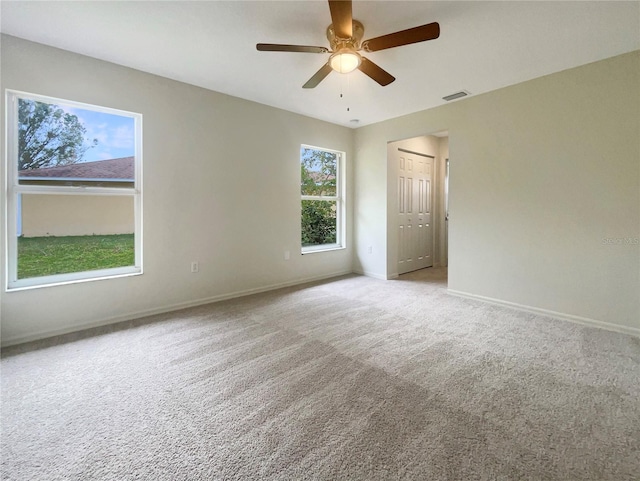 spare room featuring ceiling fan, light colored carpet, and a healthy amount of sunlight