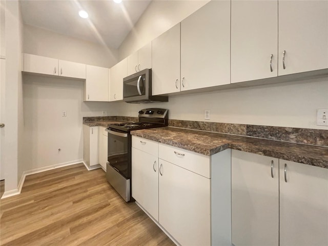 kitchen featuring stainless steel appliances, dark stone counters, light hardwood / wood-style floors, white cabinets, and lofted ceiling