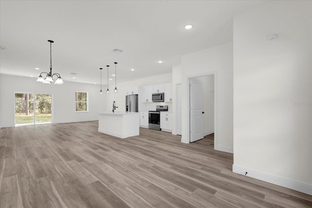 kitchen with white cabinetry, a kitchen island, a chandelier, pendant lighting, and appliances with stainless steel finishes