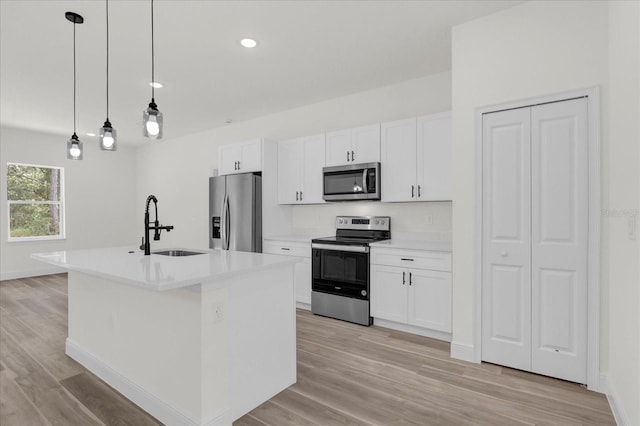 kitchen featuring a kitchen island with sink, stainless steel appliances, sink, white cabinetry, and decorative light fixtures