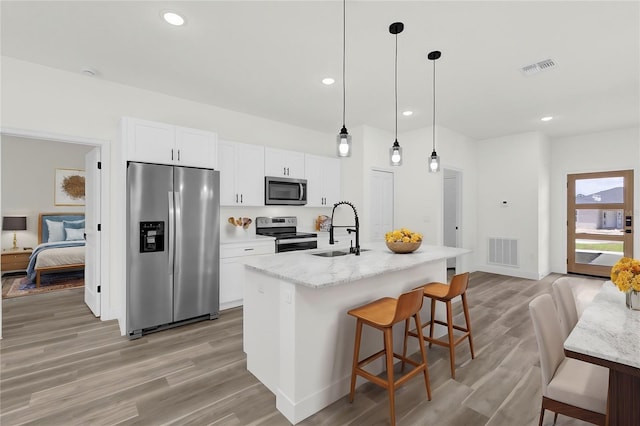 kitchen featuring stainless steel appliances, sink, white cabinetry, an island with sink, and hanging light fixtures