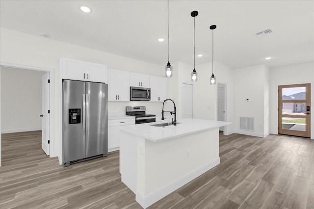 kitchen featuring a center island with sink, stainless steel appliances, sink, white cabinetry, and decorative light fixtures