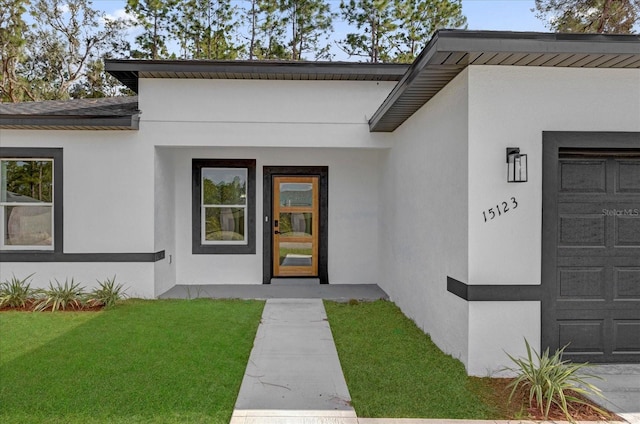 doorway to property featuring a yard, an attached garage, and stucco siding