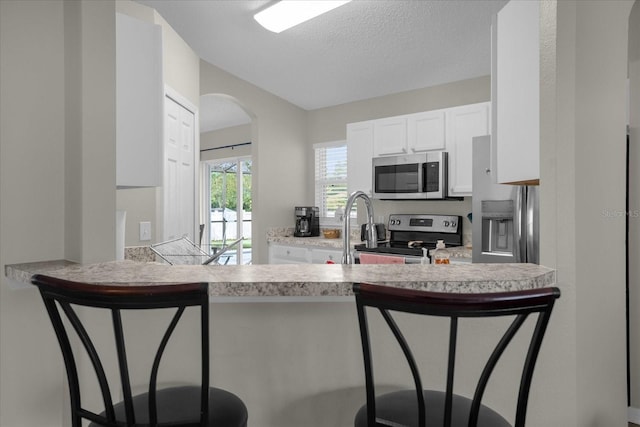 kitchen with stainless steel appliances, white cabinetry, kitchen peninsula, a kitchen bar, and a textured ceiling