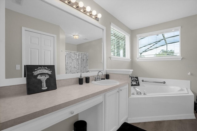 bathroom featuring vanity, tiled bath, and wood-type flooring