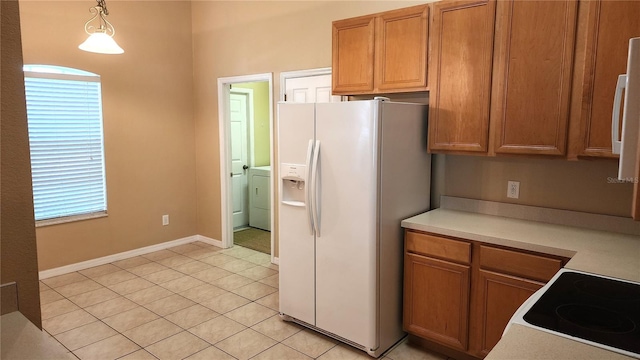 kitchen featuring white refrigerator with ice dispenser, stovetop, decorative light fixtures, washer / dryer, and light tile patterned flooring