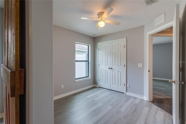 unfurnished bedroom featuring a closet, ceiling fan, light hardwood / wood-style flooring, and a textured ceiling