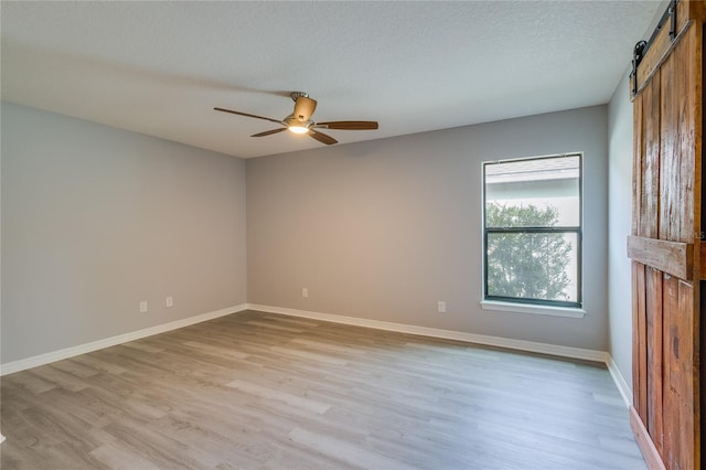 spare room with light hardwood / wood-style floors, a textured ceiling, ceiling fan, and a barn door