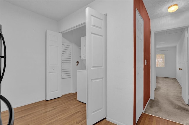 hallway with stacked washer / dryer, a textured ceiling, and light hardwood / wood-style flooring