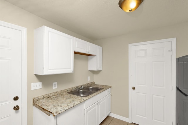 kitchen featuring light stone counters, stainless steel fridge, white cabinetry, light tile patterned floors, and sink