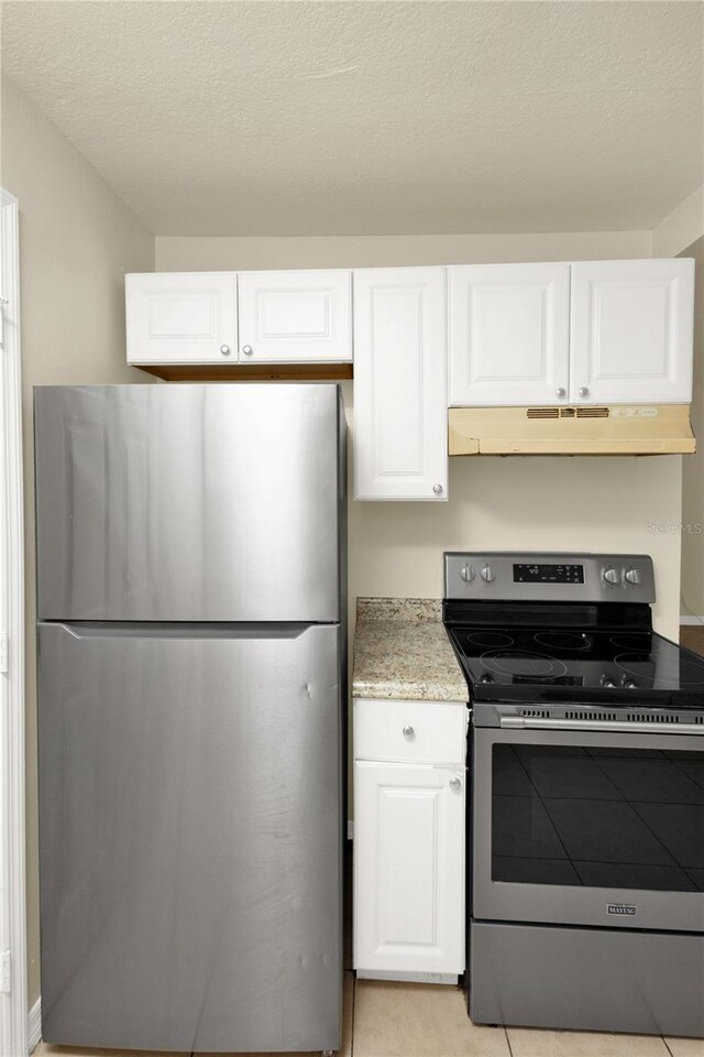 kitchen featuring light stone counters, stainless steel appliances, a textured ceiling, light tile patterned floors, and white cabinets