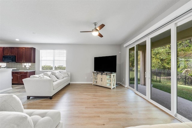 living room with light wood-type flooring, plenty of natural light, and ceiling fan