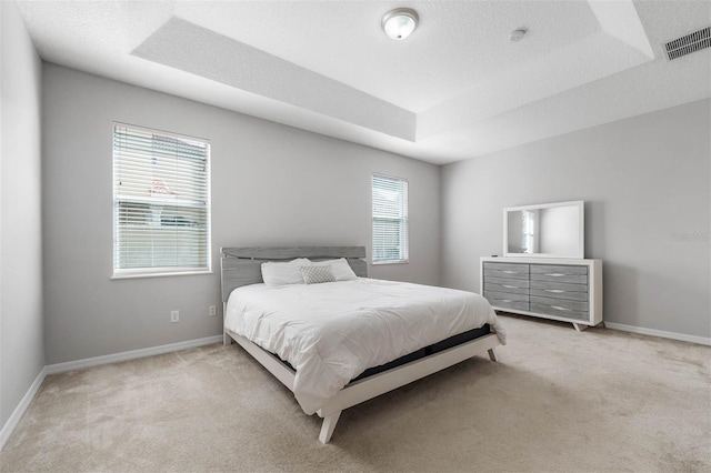 bedroom with a tray ceiling, a textured ceiling, and light colored carpet