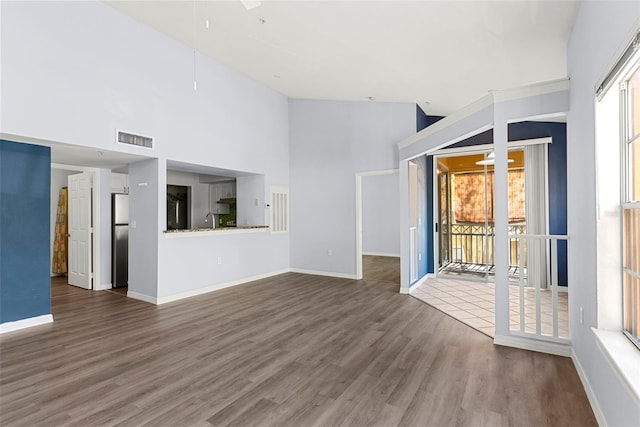 unfurnished living room featuring ceiling fan, wood-type flooring, sink, and high vaulted ceiling