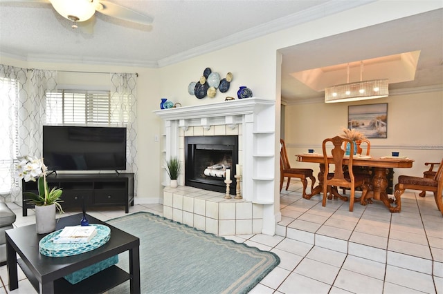 living room featuring ceiling fan, a fireplace, light tile patterned floors, and crown molding