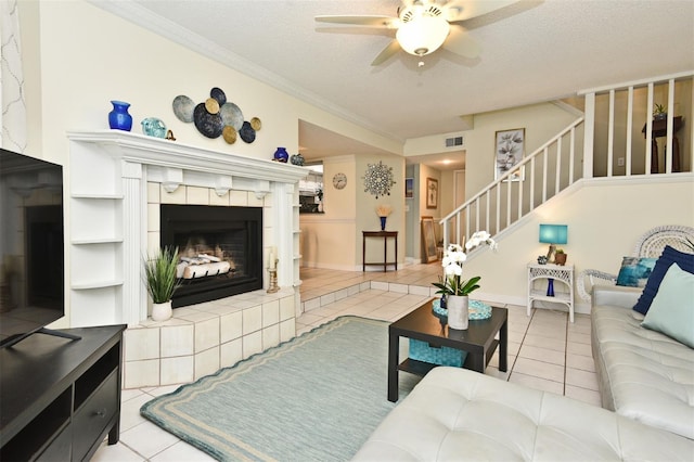 living room featuring a textured ceiling, ceiling fan, crown molding, light tile patterned floors, and a fireplace