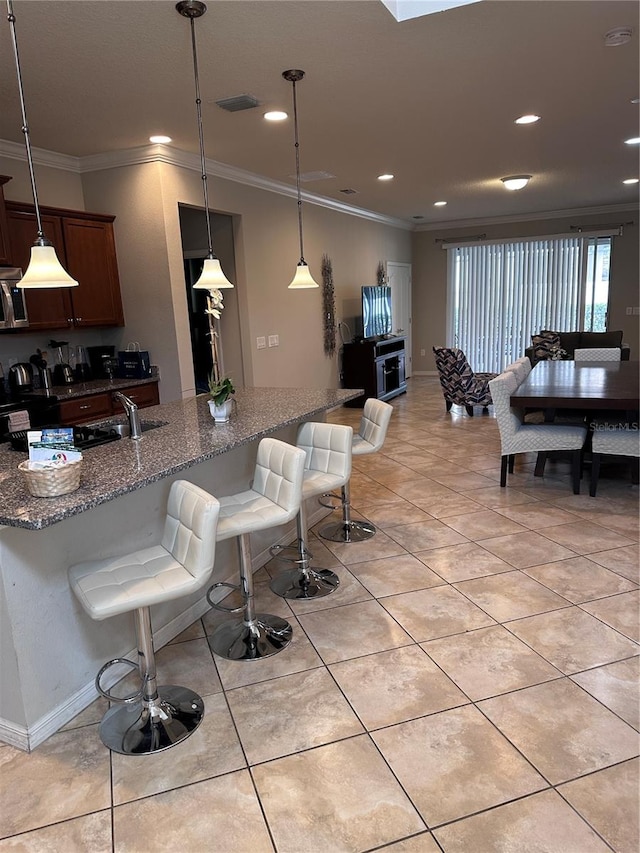 interior space with a kitchen bar, decorative light fixtures, ornamental molding, and dark stone countertops