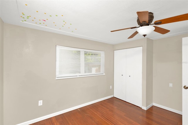 unfurnished bedroom featuring dark hardwood / wood-style flooring, ceiling fan, and a closet