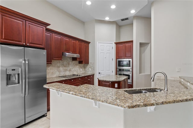 kitchen with sink, kitchen peninsula, appliances with stainless steel finishes, light stone countertops, and a breakfast bar area