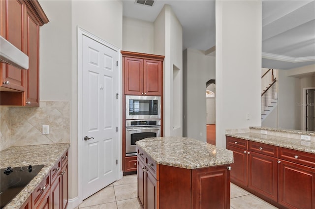 kitchen with stainless steel appliances, decorative backsplash, light tile patterned flooring, a kitchen island, and light stone countertops