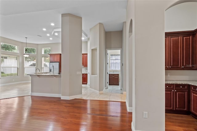 kitchen with sink, white refrigerator with ice dispenser, light stone countertops, light wood-type flooring, and decorative light fixtures