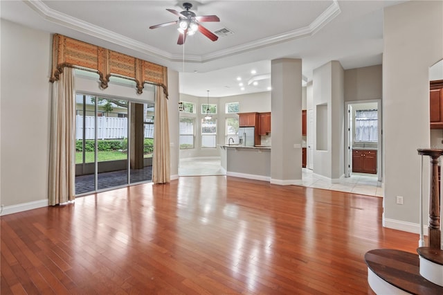 unfurnished living room featuring a tray ceiling, crown molding, and light hardwood / wood-style flooring