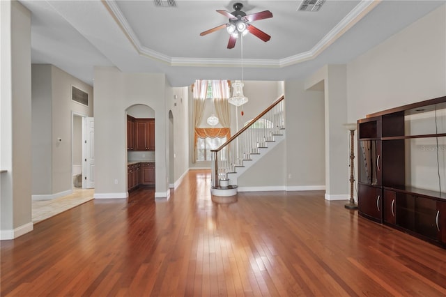 unfurnished living room featuring dark wood-type flooring, a raised ceiling, ceiling fan, and crown molding