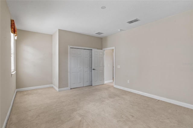 unfurnished bedroom with light colored carpet, a textured ceiling, and a closet