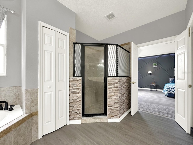 bathroom featuring independent shower and bath, lofted ceiling, hardwood / wood-style floors, and a textured ceiling