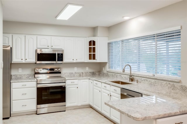 kitchen with light stone counters, kitchen peninsula, sink, white cabinetry, and appliances with stainless steel finishes