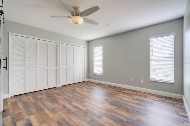 unfurnished bedroom featuring hardwood / wood-style flooring, multiple closets, and ceiling fan