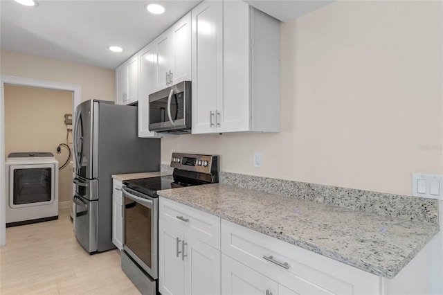 kitchen with light stone countertops, stainless steel appliances, light hardwood / wood-style flooring, white cabinets, and washer / dryer