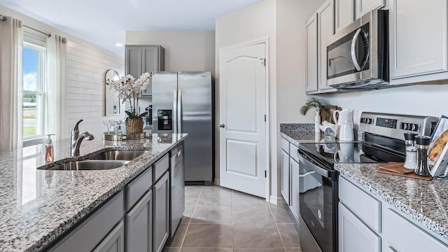 kitchen with appliances with stainless steel finishes, light tile patterned floors, gray cabinets, light stone countertops, and sink