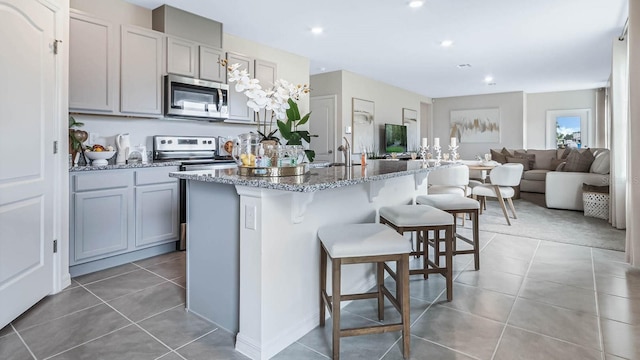 kitchen with gray cabinets, appliances with stainless steel finishes, a center island with sink, and tile patterned floors