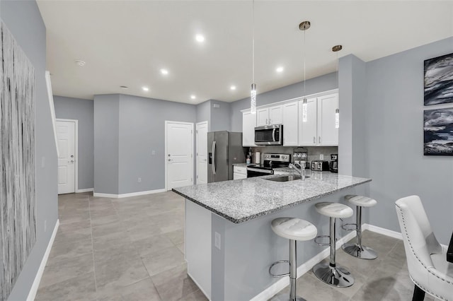 kitchen featuring white cabinetry, appliances with stainless steel finishes, decorative light fixtures, a kitchen bar, and light stone countertops