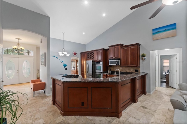 kitchen with pendant lighting, ceiling fan with notable chandelier, stainless steel appliances, decorative backsplash, and dark stone counters